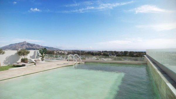 Rooftop pool with mountain views in a 3-bed apartment in San Pedro De Alcantara, Costa del Sol. Clear blue sky above modern sunbeds.