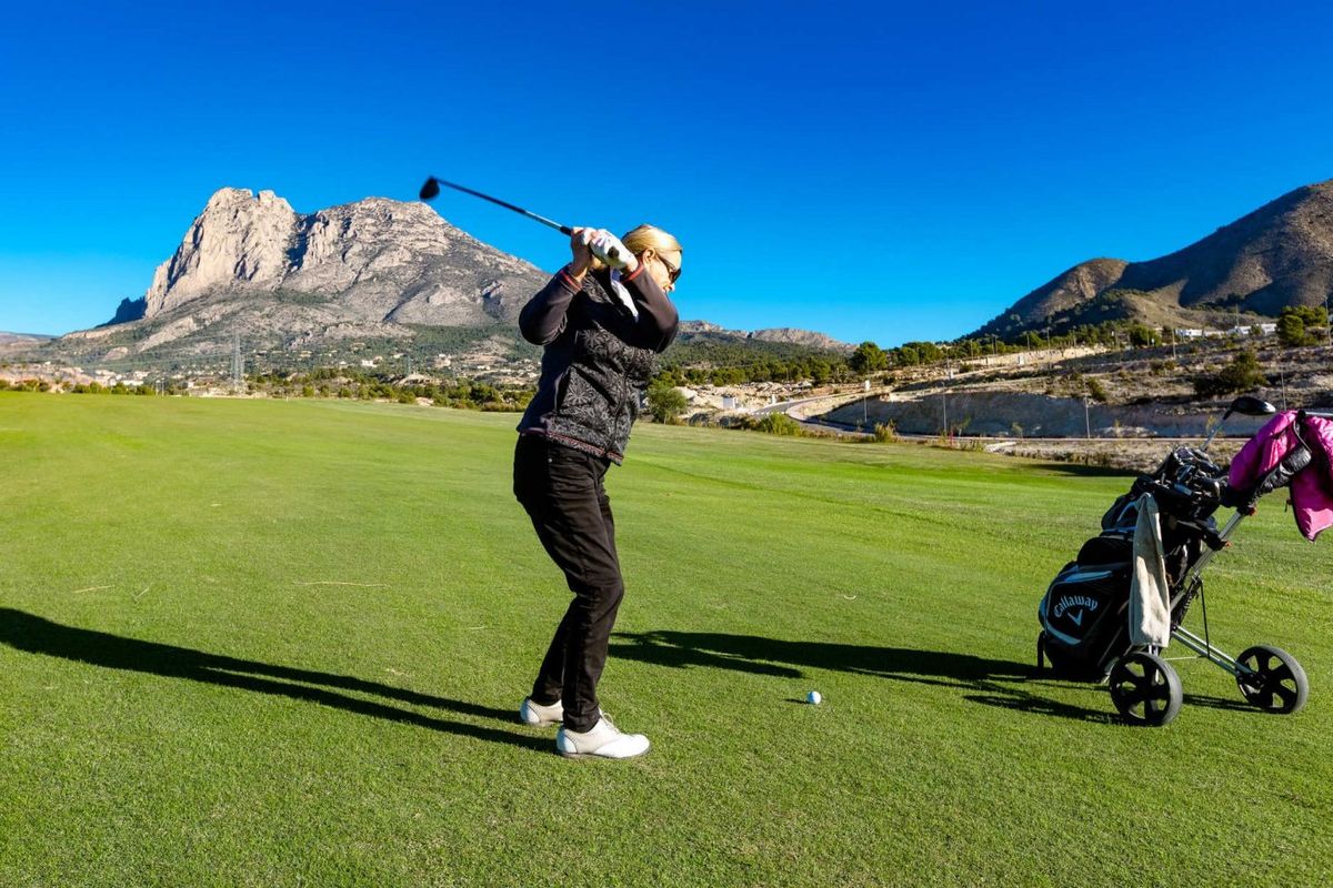 Golfer slaat af op het weelderige groene terrein nabij Finestrat, met bergen als schilderachtige achtergrond.