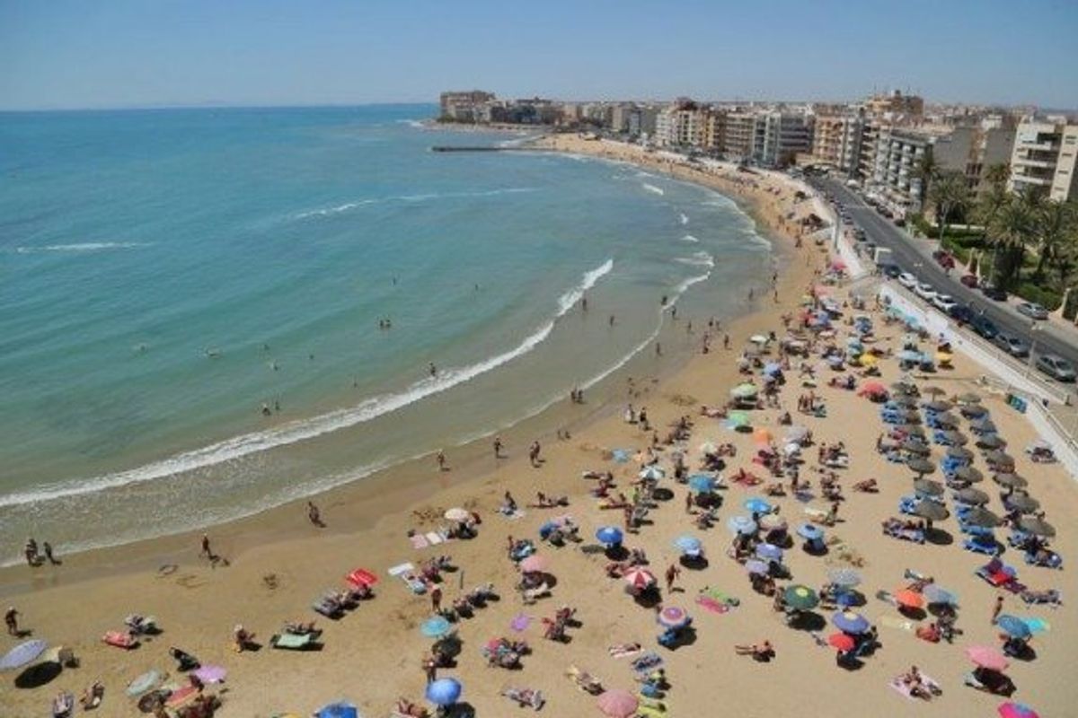 Strandzicht in Torrevieja met zonaanbidders, parasols en helder blauw water langs de zandige kust.