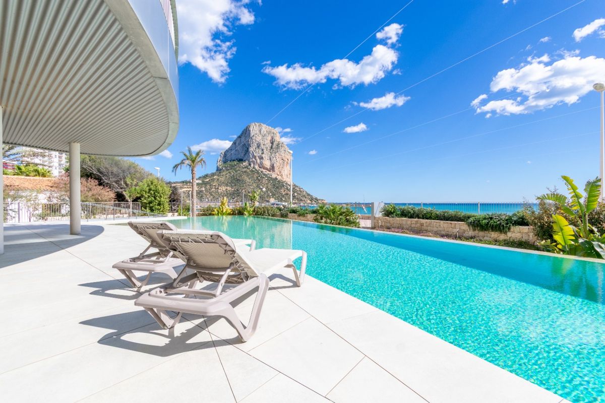 Ontspannend zwembadgedeelte met ligbedden, dat het adembenemende kustuitzicht in Calpe, Costa Blanca, laat zien.