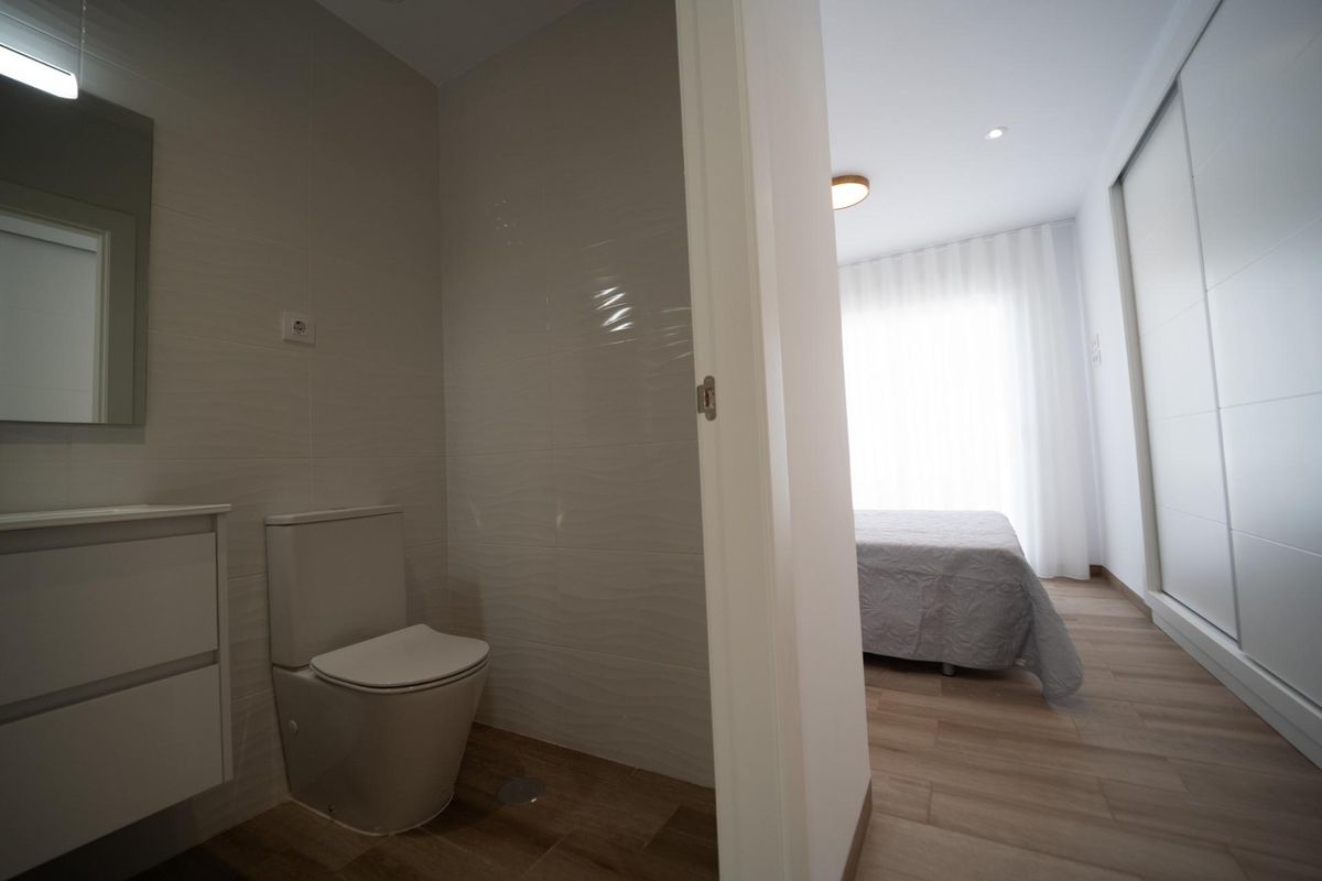 Modern bathroom leading into a bedroom, featuring toilet, sink, and tiled walls. San Javier property.
