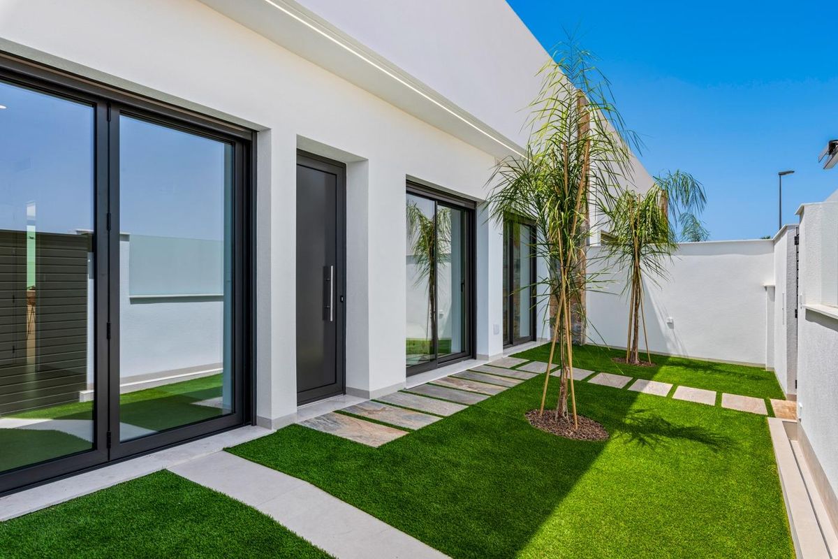 Pad langs een modern townhouse in Los Alcazares, omzoomd met gras en deuren naar binnen.