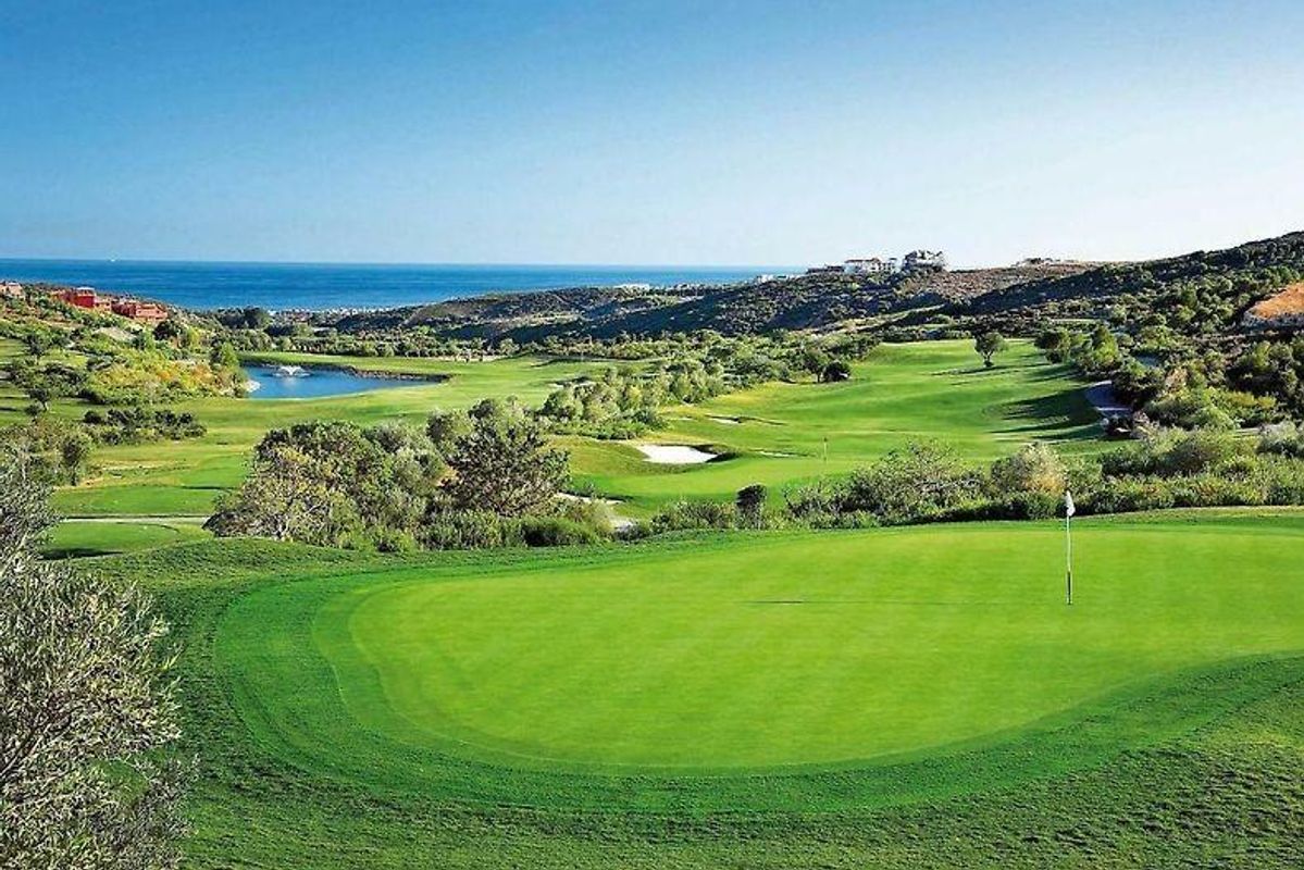 Uitgestrekte golfbaanzicht in Estepona met glooiende heuvels en het rustige water van het meer.
