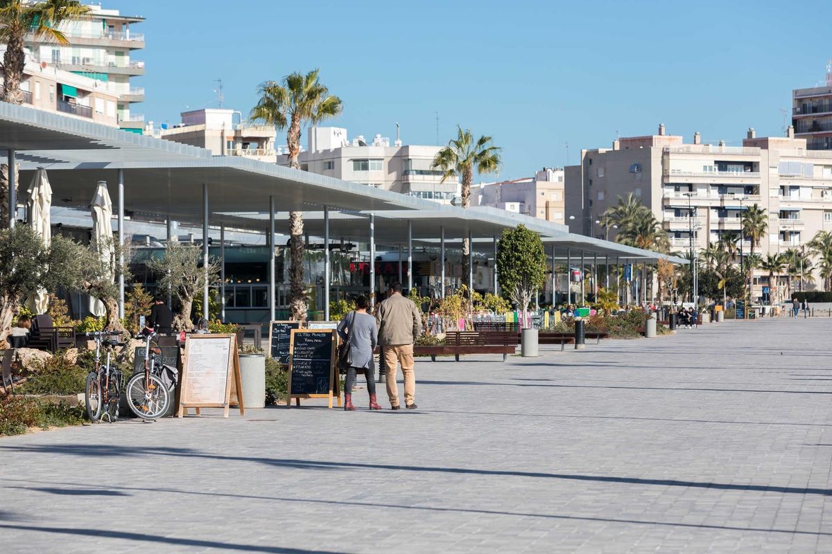 Promenade in Santa Pola vol winkels en restaurants, met palmbomen en een levendige sfeer.