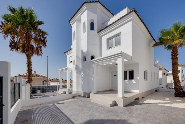 Exterieur van de moderne villa in San Fulgencio met palmbomen en een heldere blauwe lucht.