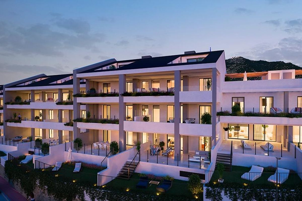 Buitenzicht op een stijlvol appartementencomplex bij schemering in Benalmádena, met verlichte balkons.