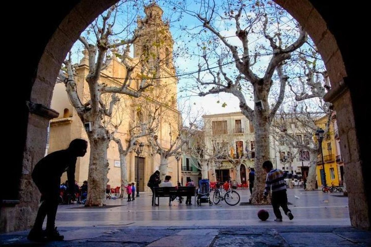 Een pittoresk tafereel in Aspe, met een levendige plein waar mensen spelen en bomen de paden omzomen.