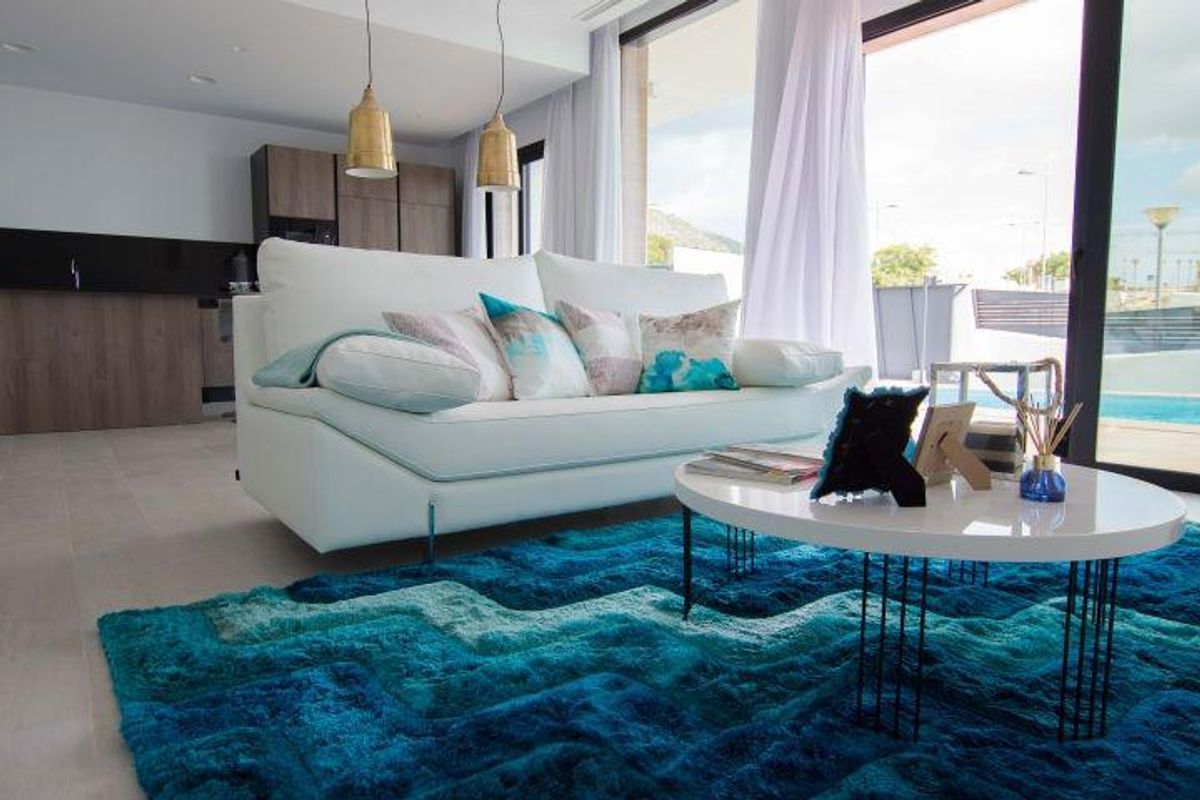 Moderne woonkamer met turquoise vloerkleed en zicht op zwembad in villa aan de Costa Blanca
