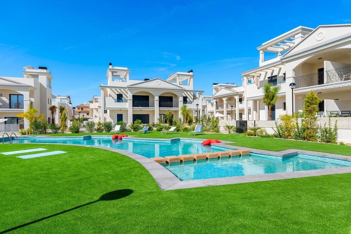 Bodemzicht van appartementen in Rojales met pool en ligstoelen op het groene gras.