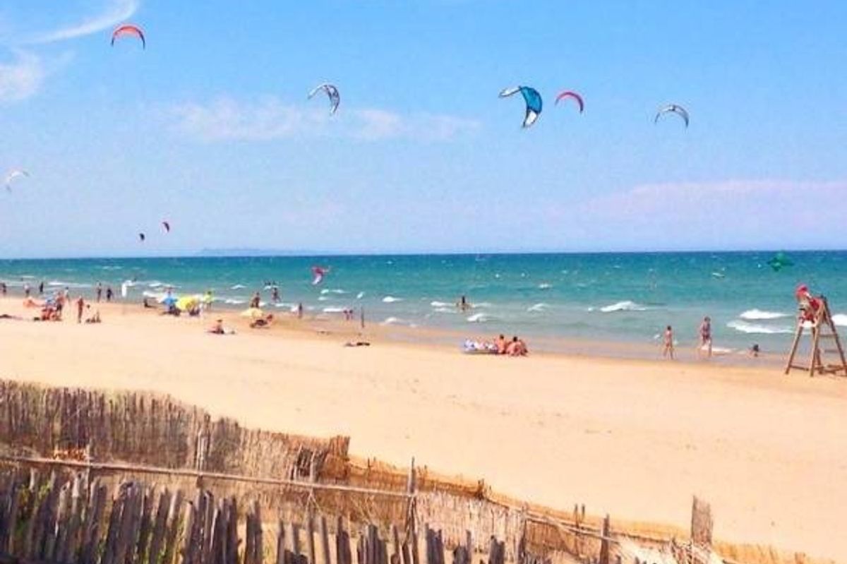 Beach in Denia filled with sunbathers and colorful kites on a sunny day.