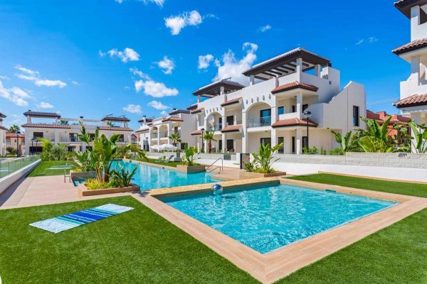 Exterior view of a modern town house complex in Rojales, featuring pools and landscaped gardens.