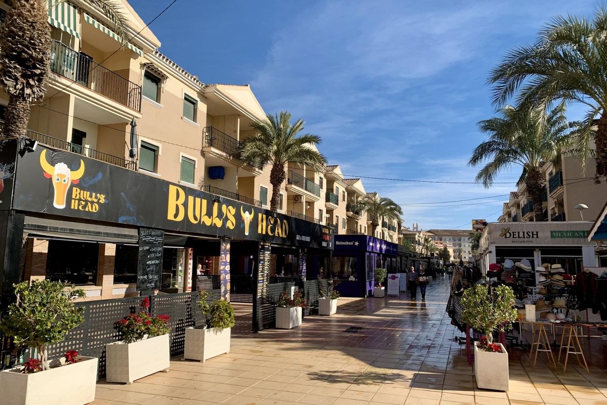 Straat met winkels en restaurants in Los Alcazares, met buitenzitplaatsen en palmbomen.