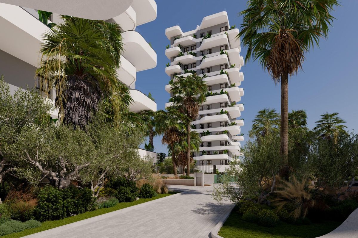 Lush gardens and palm trees leading to the entrance of a modern apartment complex in Calpe, Costa Blanca North.
