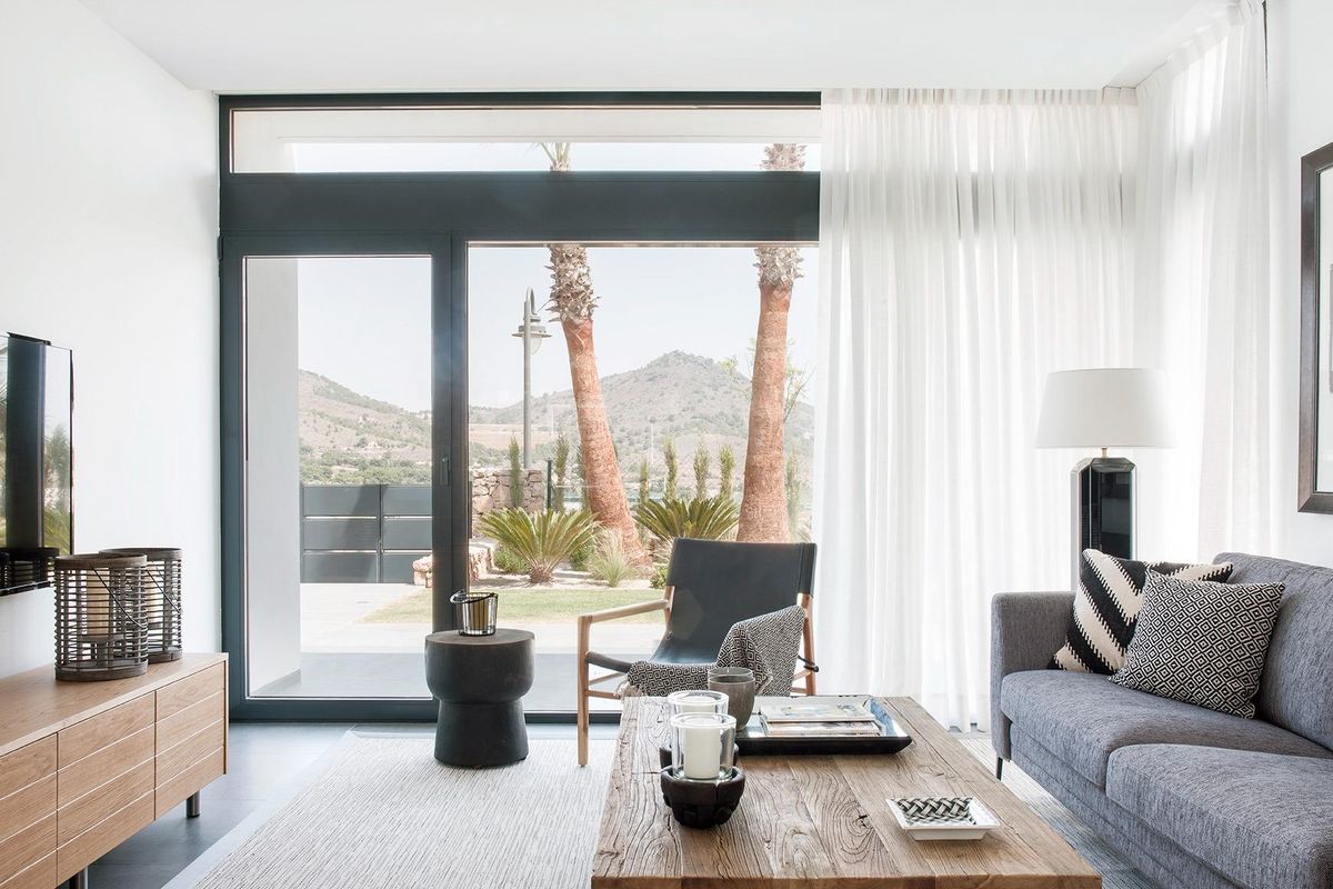 Woonkamer met grote ramen en uitzicht op palm bomen in de 4-slaapkamer villa in La Manga Club, Spanje.