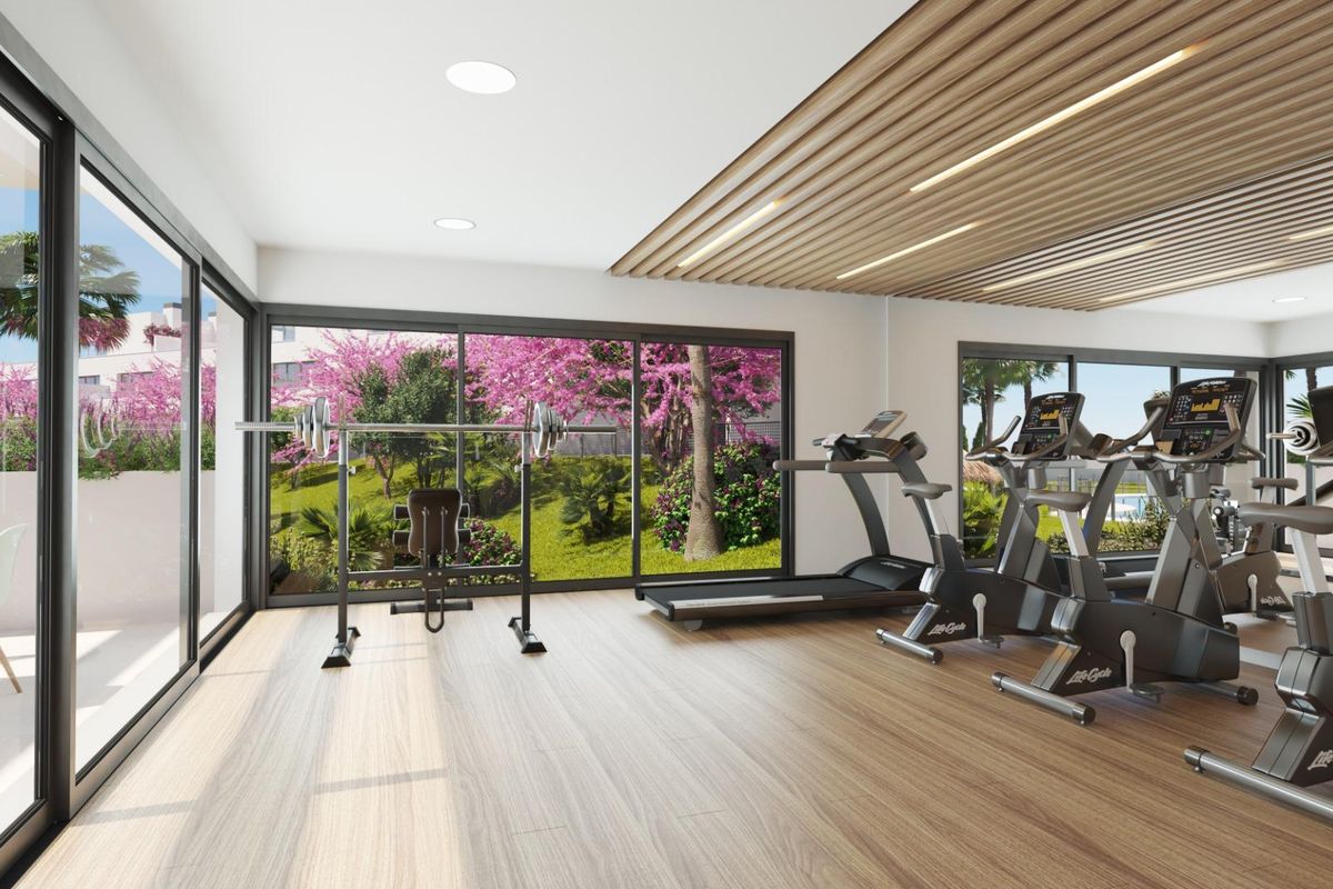 Moderne sportschool met fitnessapparatuur en grote ramen met uitzicht op tuinen in Estepona, Costa del Sol.