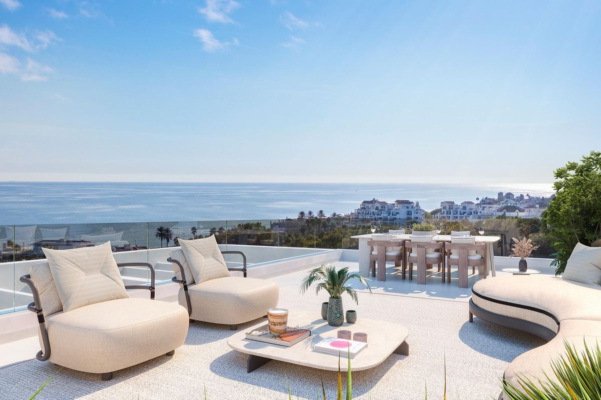 Heldere terras van een appartement op de begane grond in Estepona, met uitzicht op zee en uitnodigende stoelen.