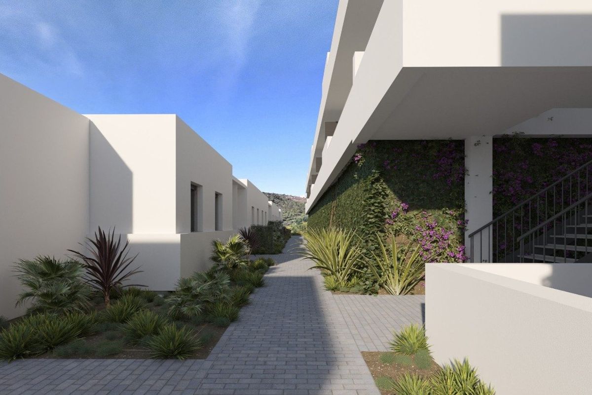 Landscaped walkway between modern white townhouses in Manilva, Costa del Sol, featuring lush plants and exterior stairs.