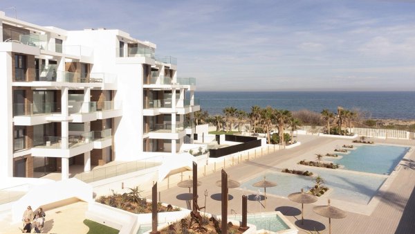 Buitenzicht op een modern penthousecomplex in Denia, met zwembaden en palmbomen aan het strand.