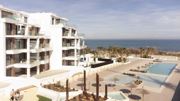 Buitenzicht op een modern penthousecomplex in Denia, met zwembaden en palmbomen aan het strand.