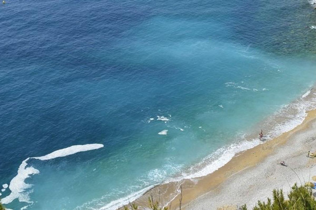 Luchtfoto van een strand nabij Benitachell, met kristalhelder water en ligbedden.