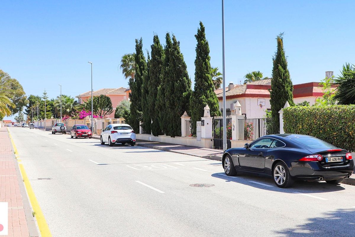 Straatbeeld in San Fulgencio met villa's en geparkeerde auto's onder een heldere lucht.