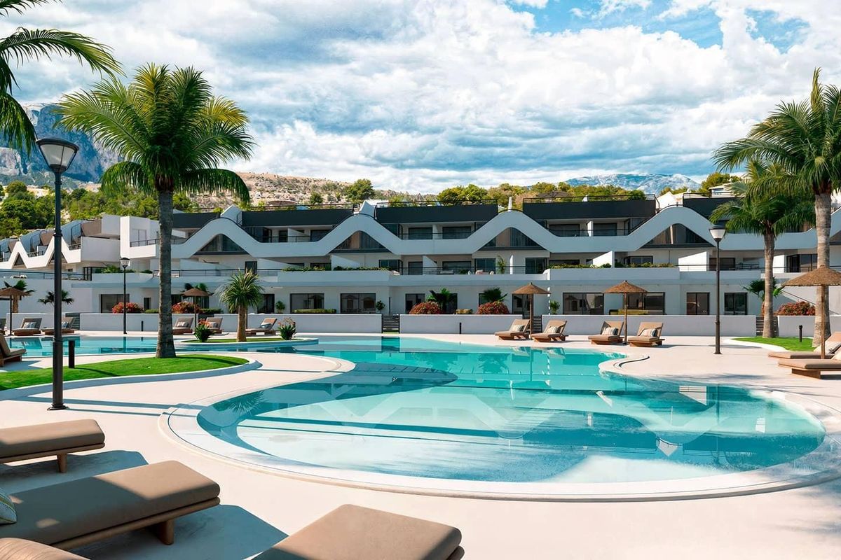 Heldere zwembadzone bij het appartementcomplex met ligstoelen en palmbomen in Alfas del Pi.