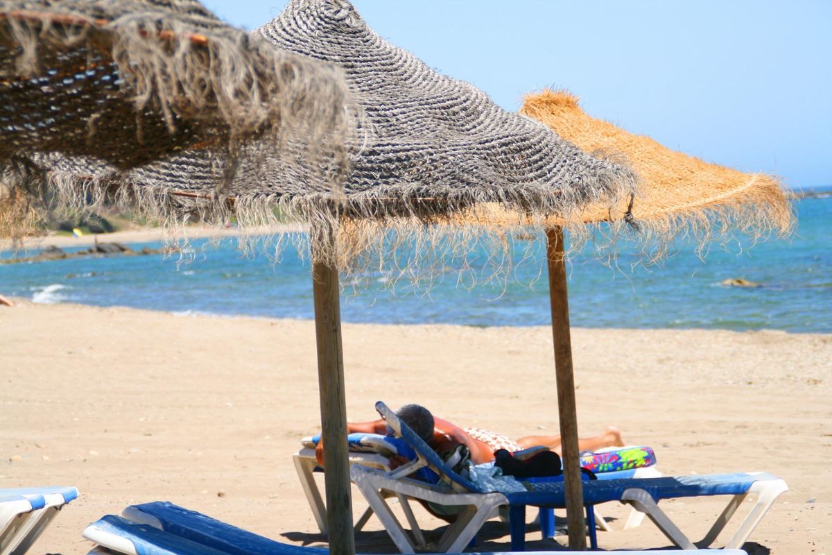 Zonaanbidders onder rieten parasols op een strand in Mijas, Costa del Sol, Spanje.