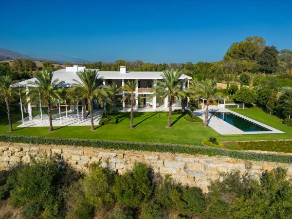 Luchtfoto van een moderne villa met palmbomen, zwembad en weelderige tuin in Casares, Costa del Sol.