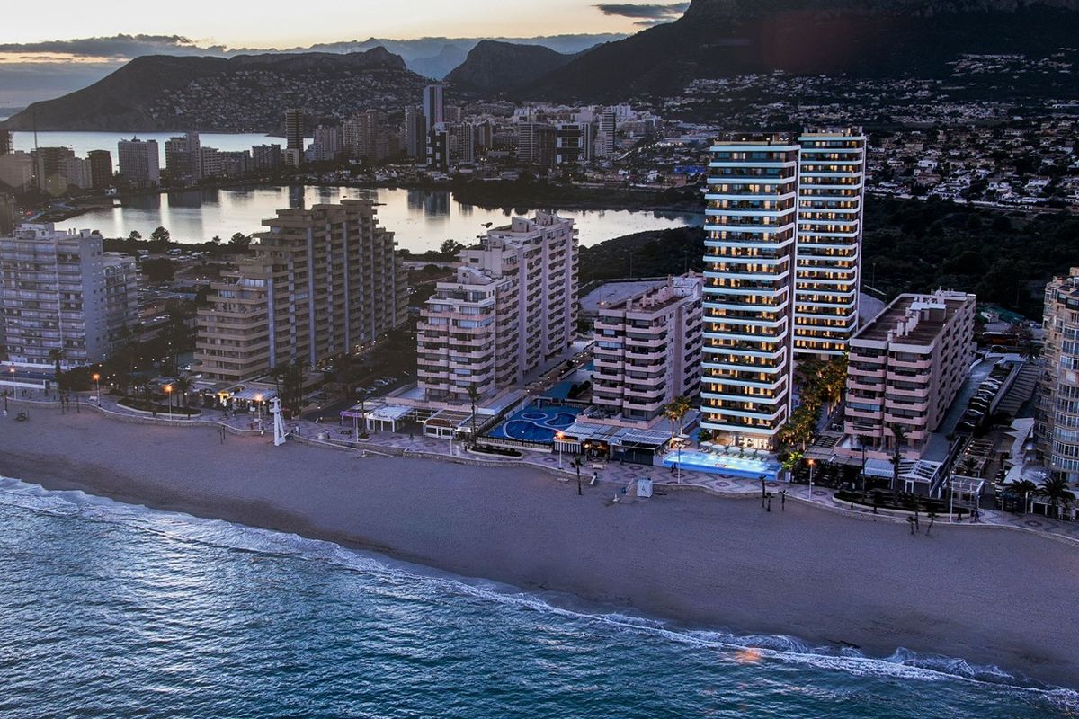 Schemerige foto van het strandappartementcomplex in Calpe, met verlichte gebouwen langs de kust.