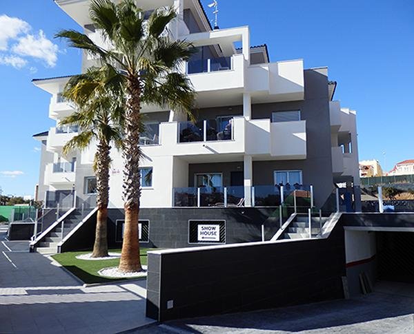 Buitenzicht op een modern 2-slaapkamerappartement in Orihuela Costa, met palmbomen en een stijlvolle gevel.