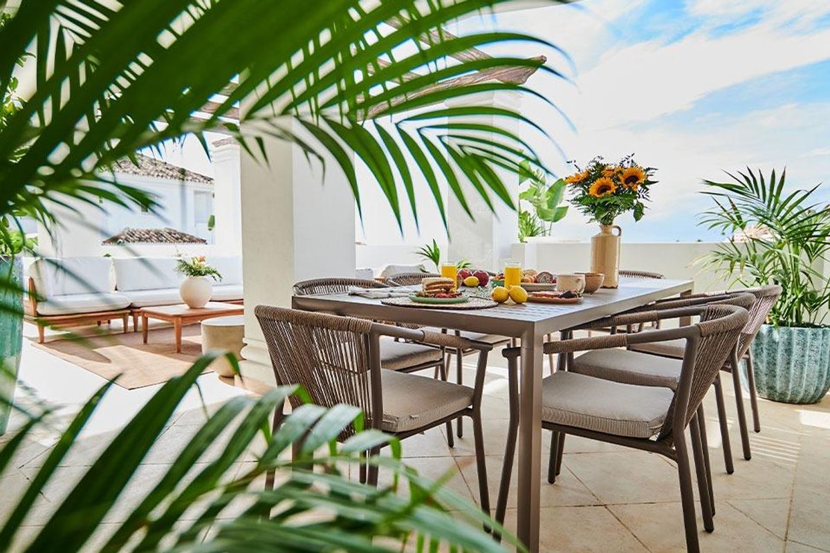 Heldere eetruimte buiten met een tafel voor het ontbijt en weelderige groene planten in een penthouse in Marbella.