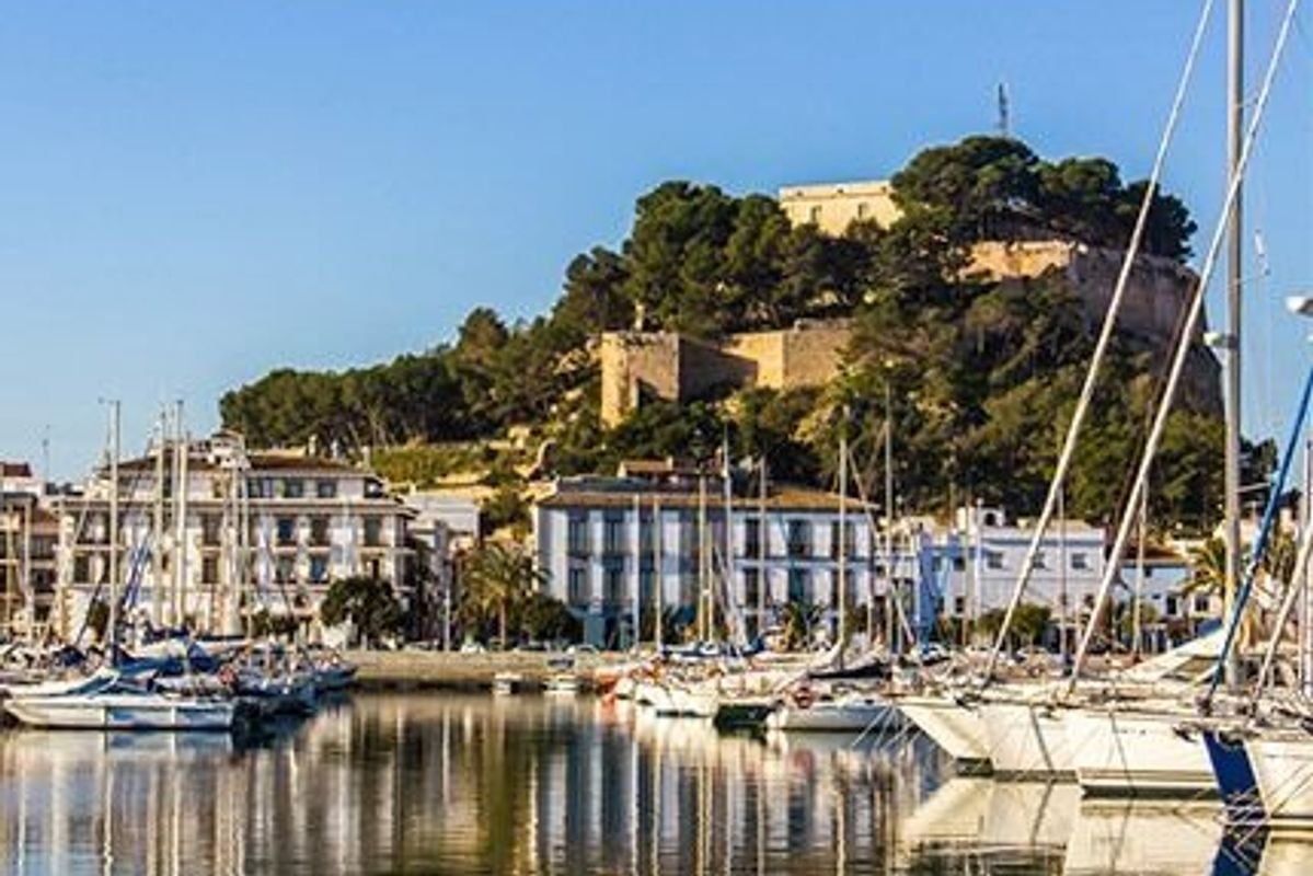 Scenic view of Denia marina featuring boats and waterfront buildings on a sunny day.
