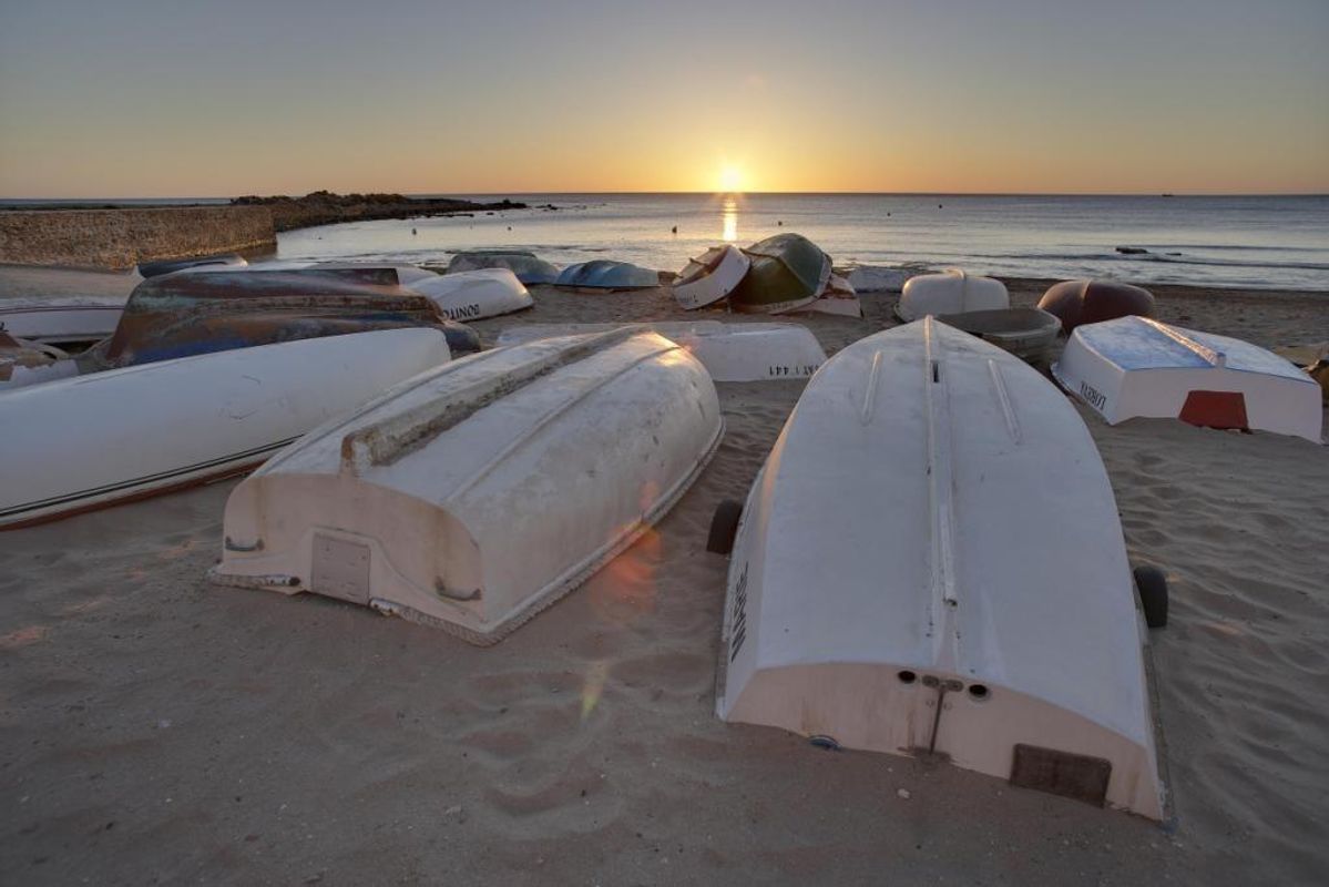 Geverfde boten op het strand bij zonsondergang, wat een rustige scène creëert aan de kust nabij het strand van Torrevieja.