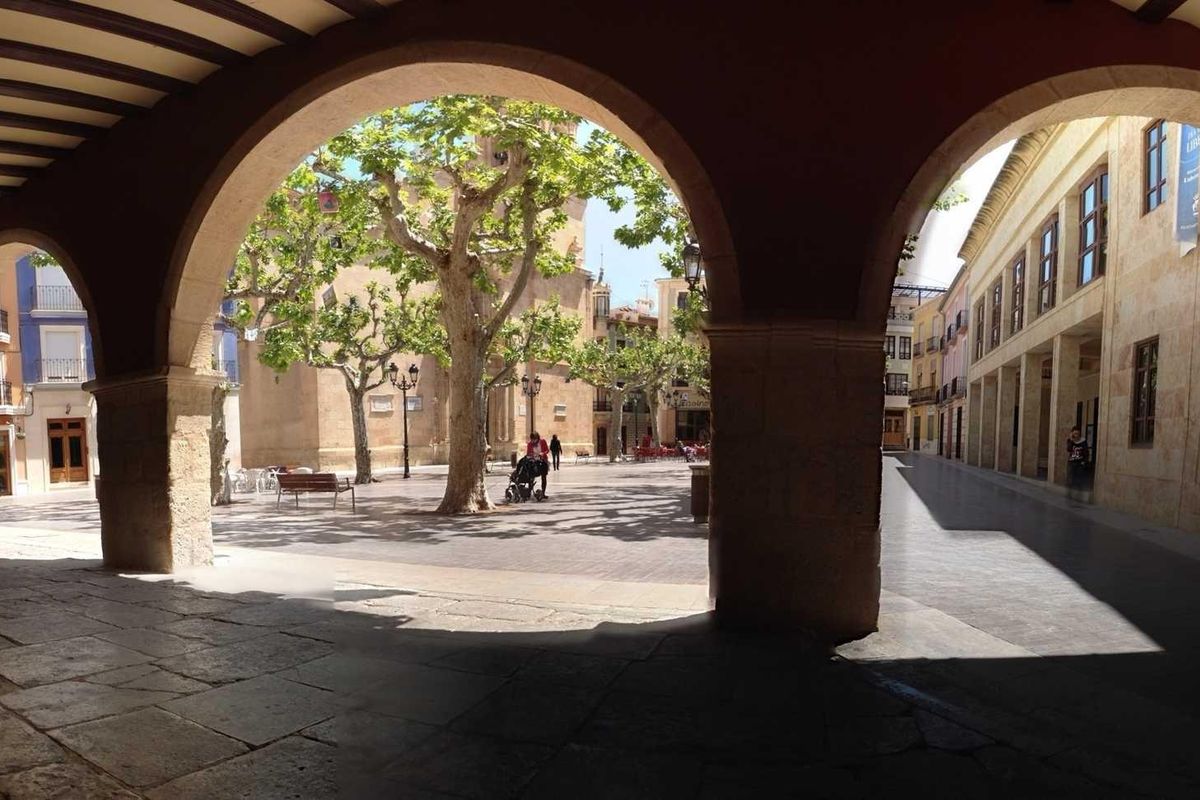 Charmante boog die een levendige plein in Aspe omlijst, met mensen die wandelen en bomen langs de straten.