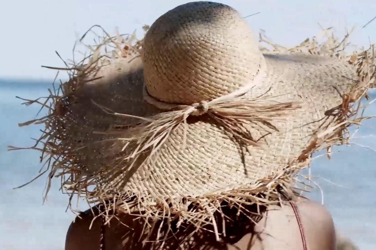 Vrouw in een strohoed op een strand in Spanje, genietend van de zon en zeezicht nabij Torrevieja.