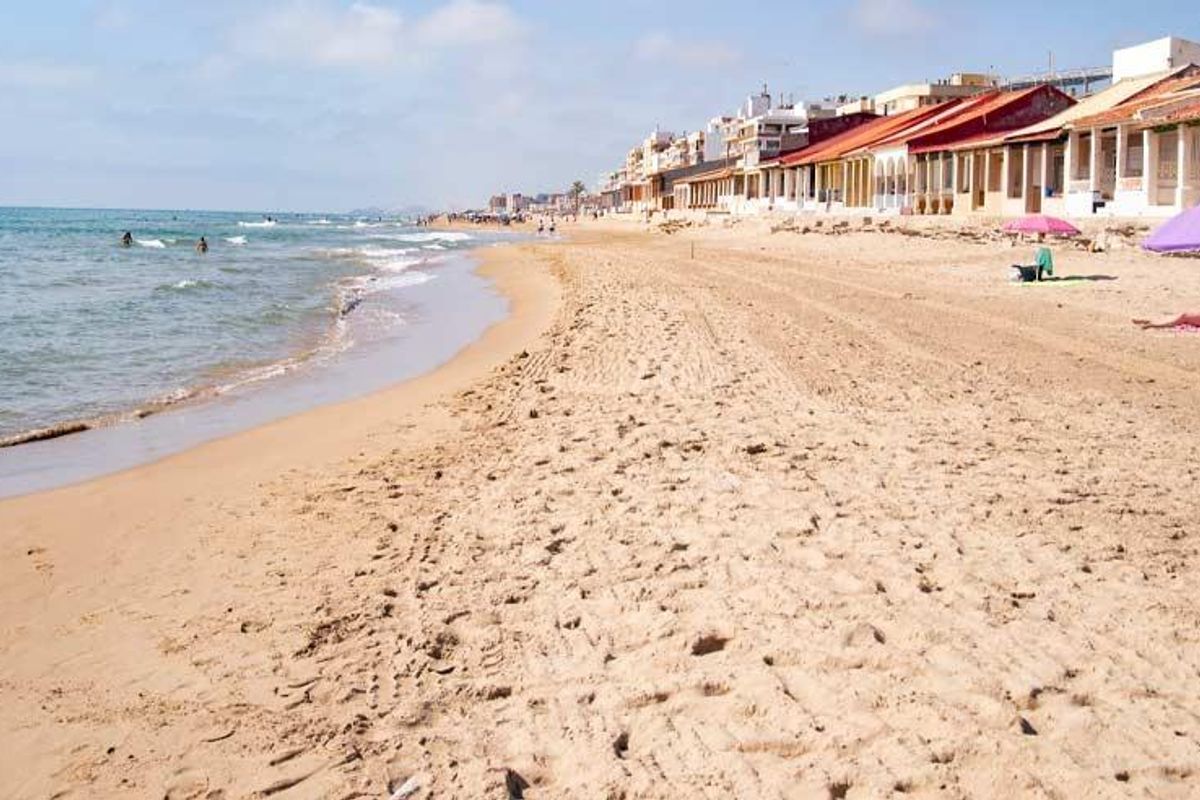 Zandstrand van Guardamar del Segura met strandgangers die onder parasols ontspannen.