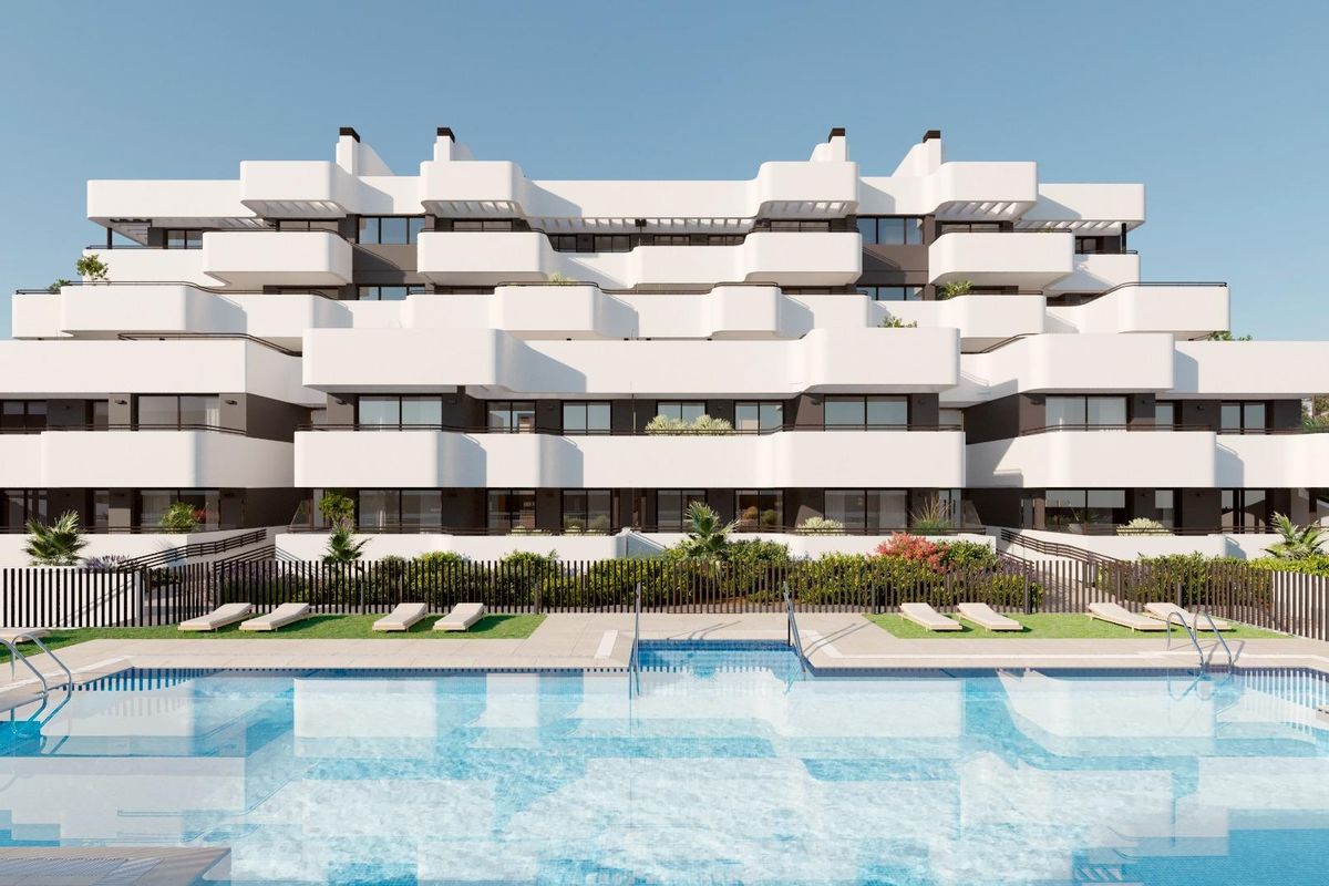 Exterieur van een modern wit appartementencomplex met een zwembad ervoor, gelegen in estepona, spanje. ligstoelen staan langs het zwembad.