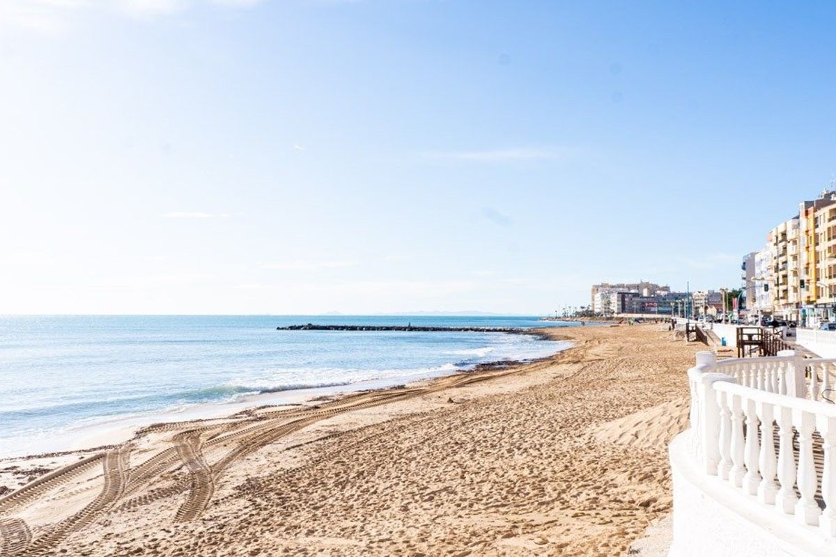 Brede opname van het zandstrand in Torrevieja, met helder water en gebouwen aan het strand op de achtergrond.