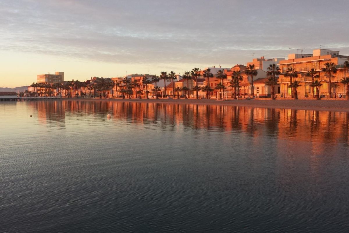 Serene uitzicht op het strand van Los Alcazares bij zonsondergang, met warme kleuren weerkaatst op het rustige water.