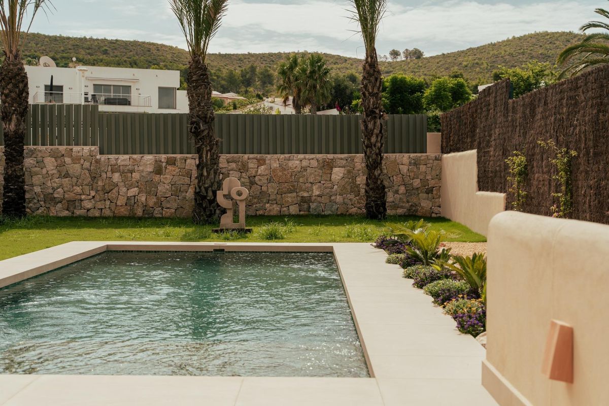 Uitzicht op het zwembad vanuit de tuin, omringd door palmbomen en een stenen muur in Jávea.