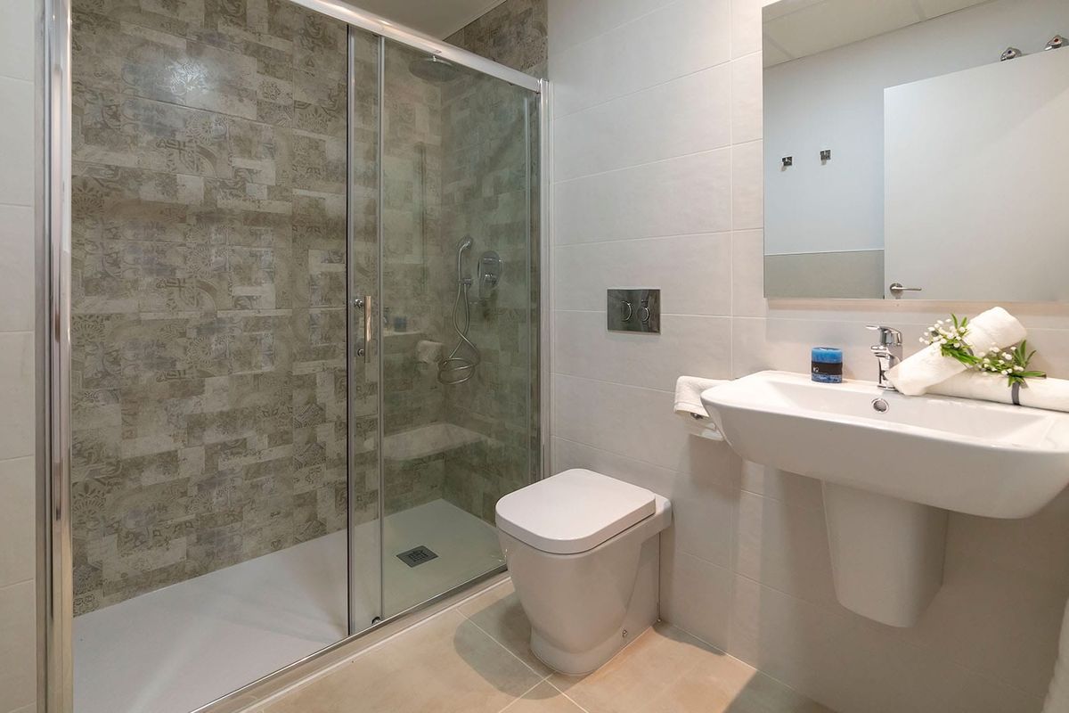 Moderne badkamer met glazen douche, witte voorzieningen en gestructureerde grijze betegelde muur in woning in Mar de Pulpi