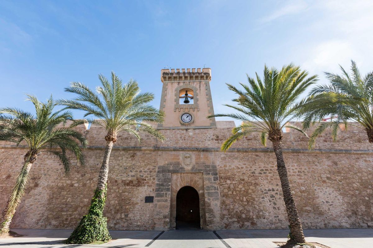 Historische kloktoren omringd door palmen in Santa Pola, die de charmante architectuur van de stad laat zien.
