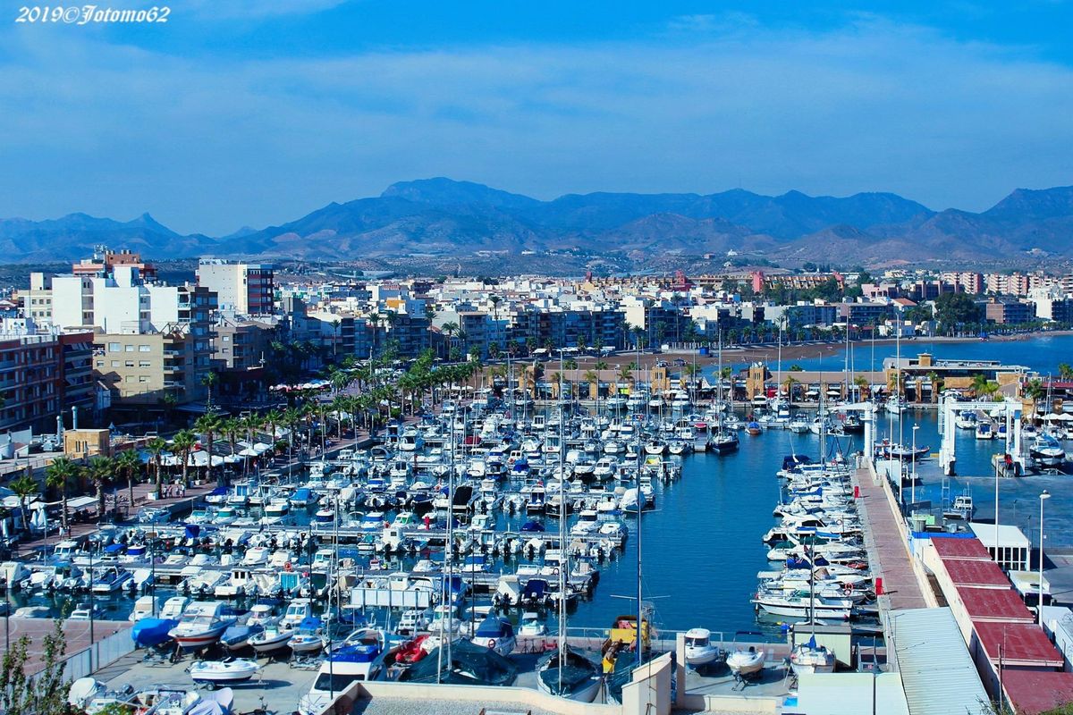 Uitzicht op de haven van Fuente Álamo met boten en gebouwen, die de levendige haven sfeer toont.