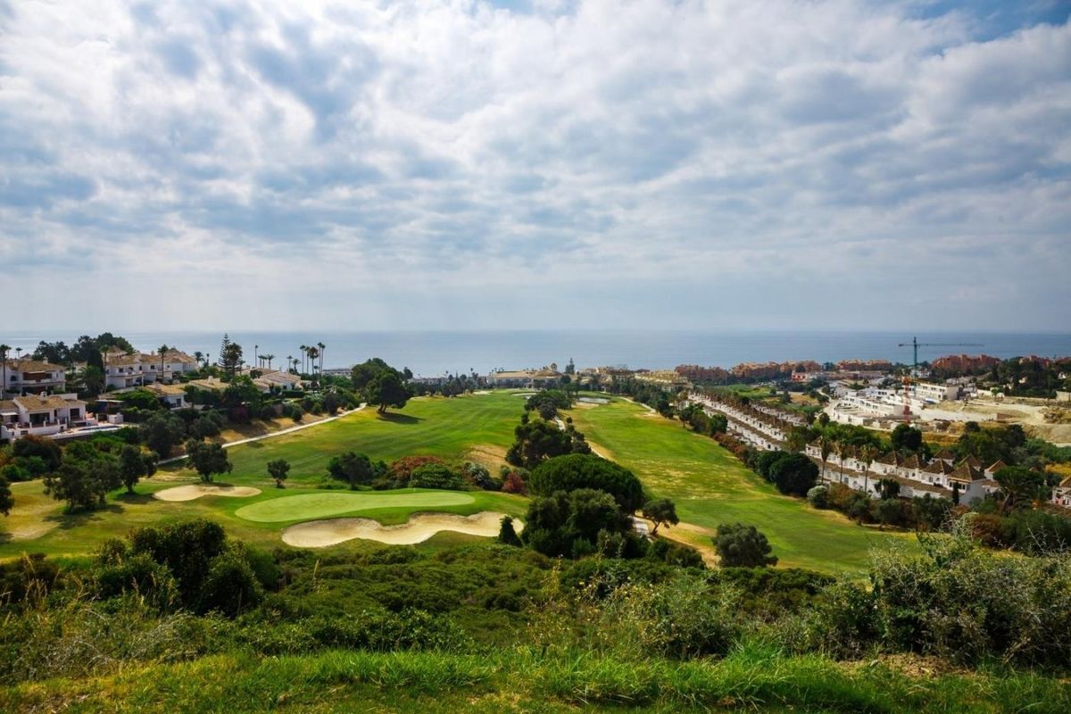 Panoramisch zicht op een weelderige groene golfbaan met zandbunkers, kusthuizen en oceaanhorizon in Manilva