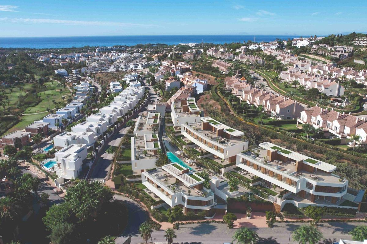 Luchtfoto van moderne townhouses in Estepona met zwembaden en groene ruimtes, met uitzicht op de kust.