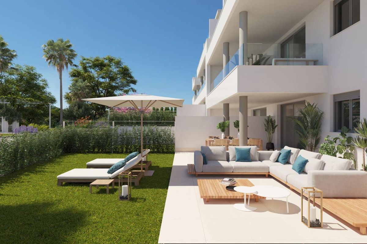 Terras van begane grond appartement met witte buitenbank, houten salontafel en weelderige groene tuin in Mijas