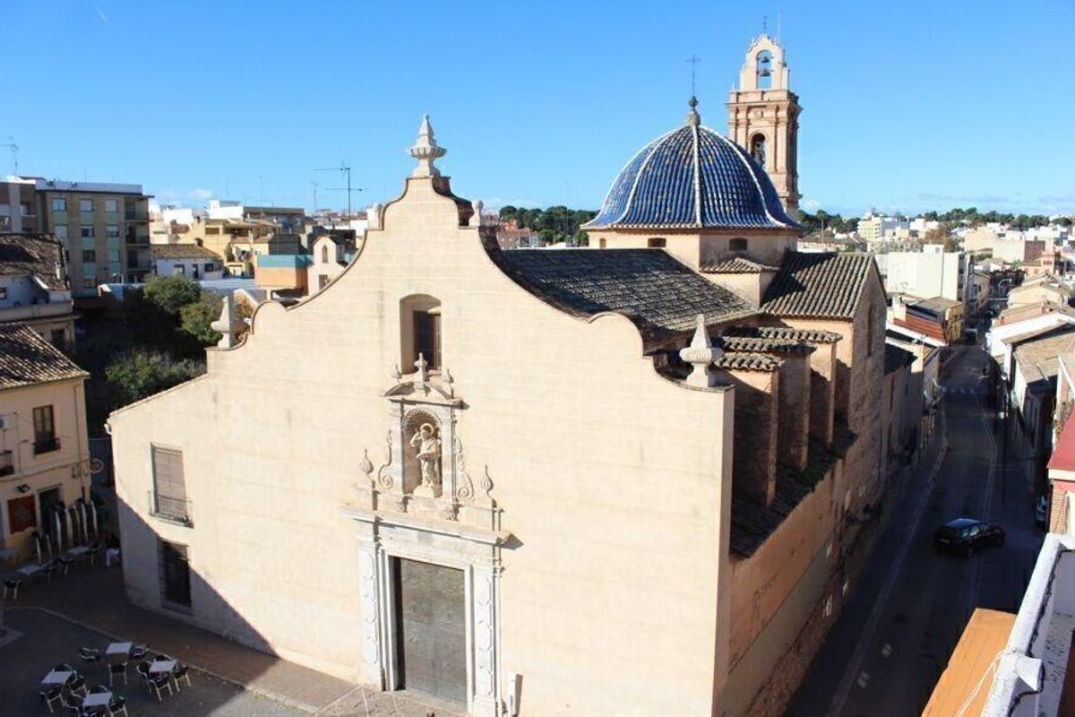 Dichtbij van een historische kerk in Godella, met complexe architectuur en een levendige blauwe koepel tegen een heldere lucht.