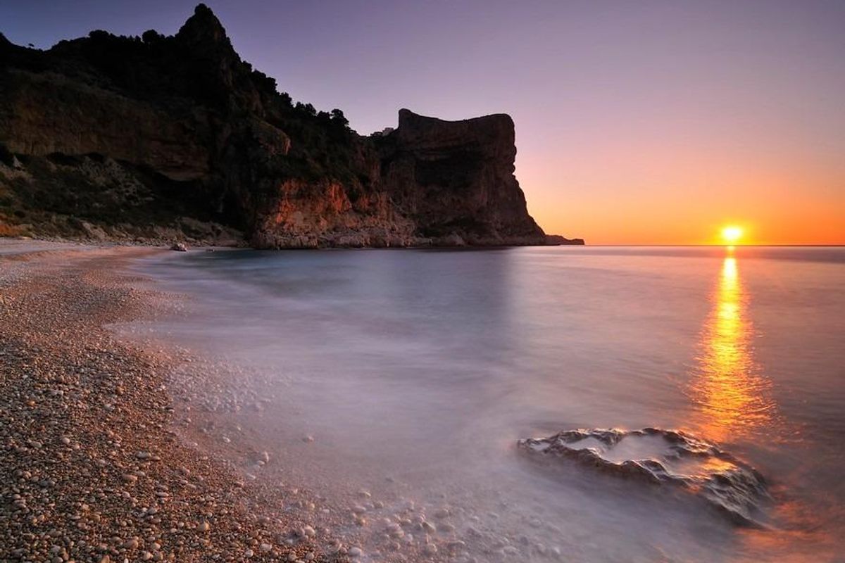 Zonsondergang over het rustige strand, dat de natuurlijke schoonheid van Benitachell, Costa Blanca Noord, toont.