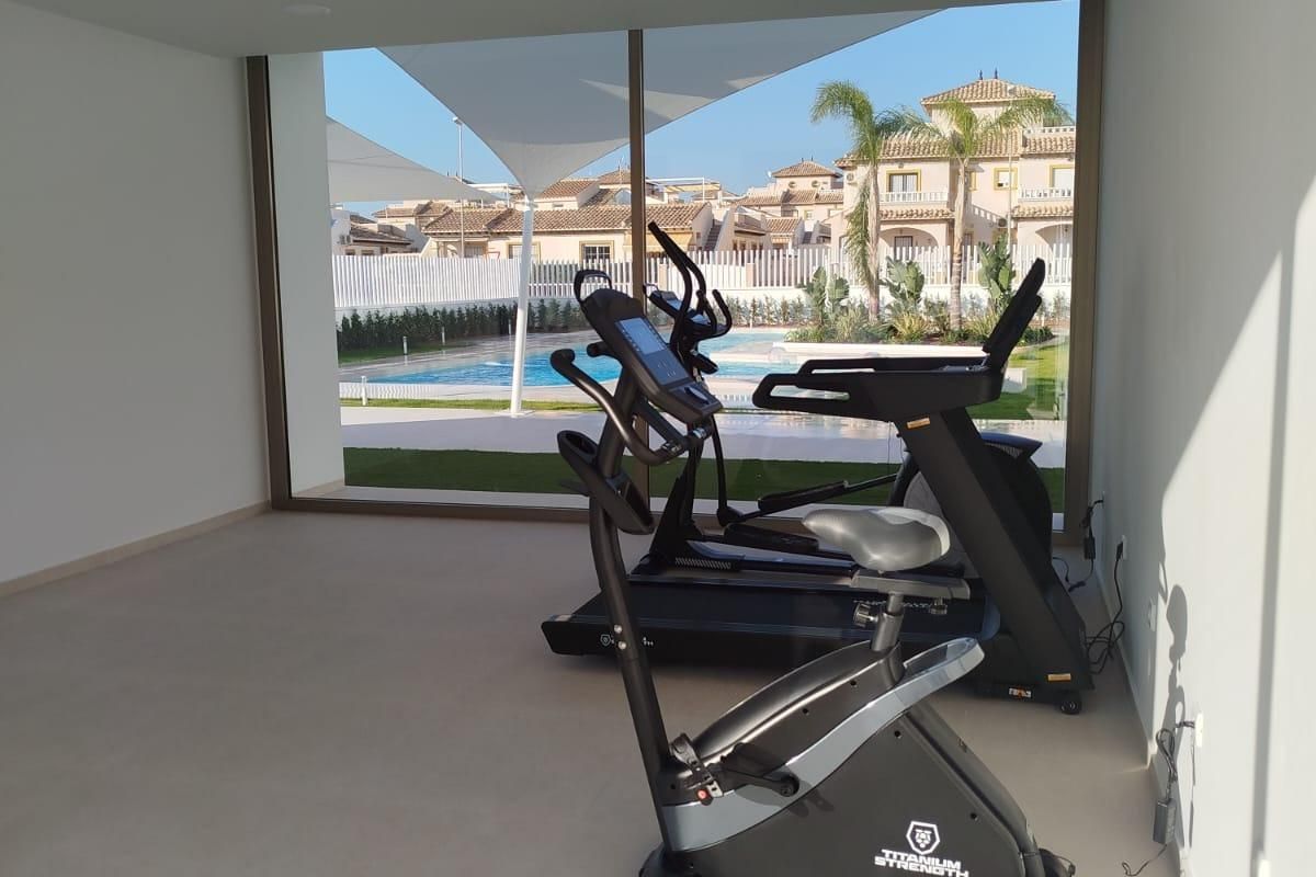 Heldere sportschool met fitnessapparatuur met uitzicht op het zwembad in Orihuela Costa, Costa Blanca Zuid.