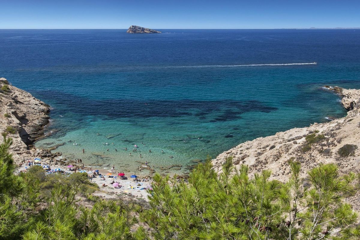 Afgelegen baai met turquoise water en strandgangers die een zonnige dag in Costa Blanca genieten.